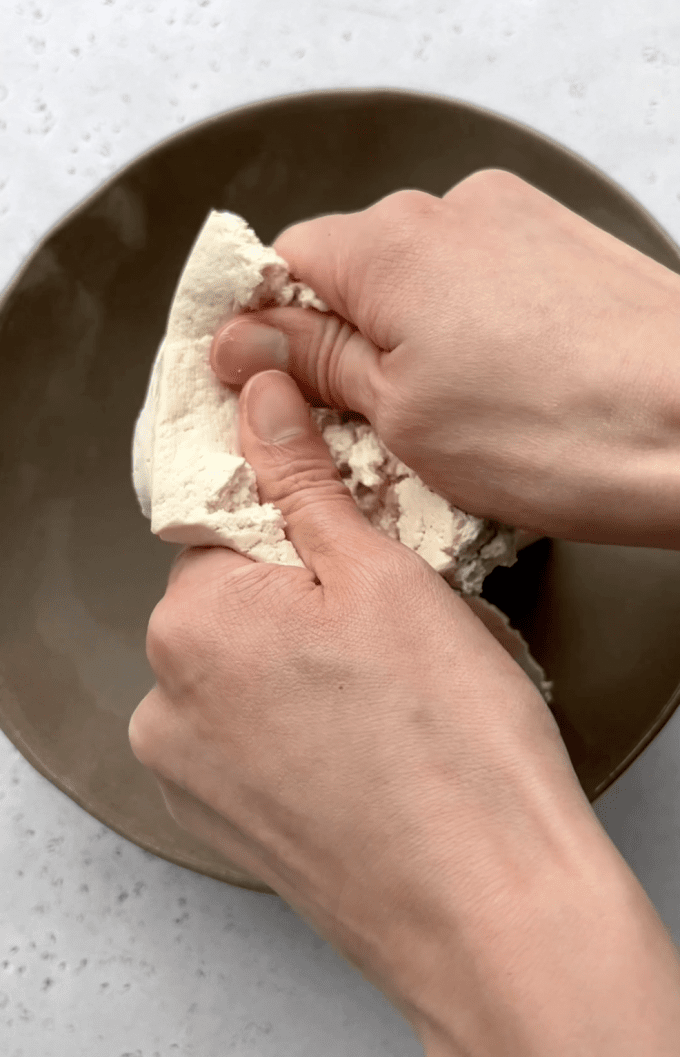 Crumbling a block of firm tofu with hands.