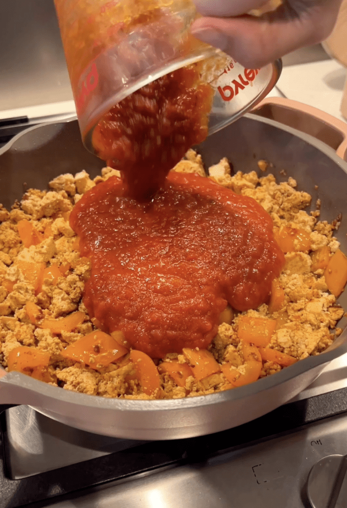 Tomato sauce being added to tofu-vegetable mixture.