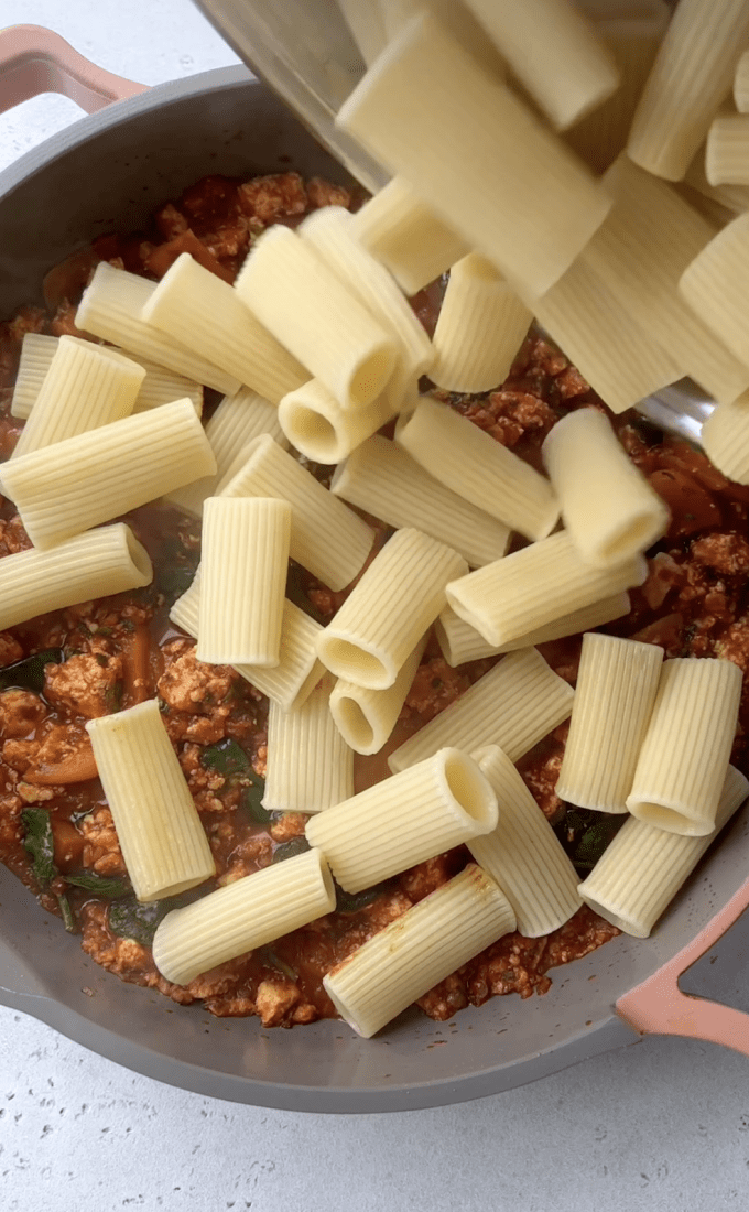 Cooked pasta being added to tofu tomato pasta sauce.