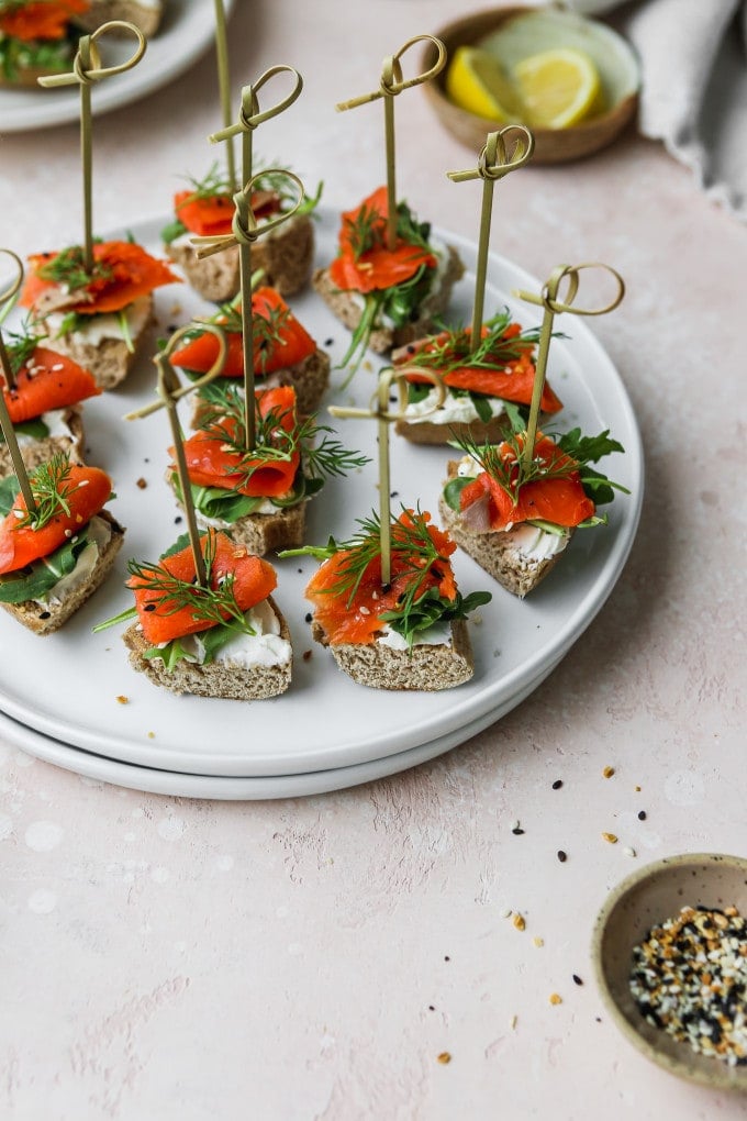 Smoked salmon appetizer bagel bites with skewers on a white plate.