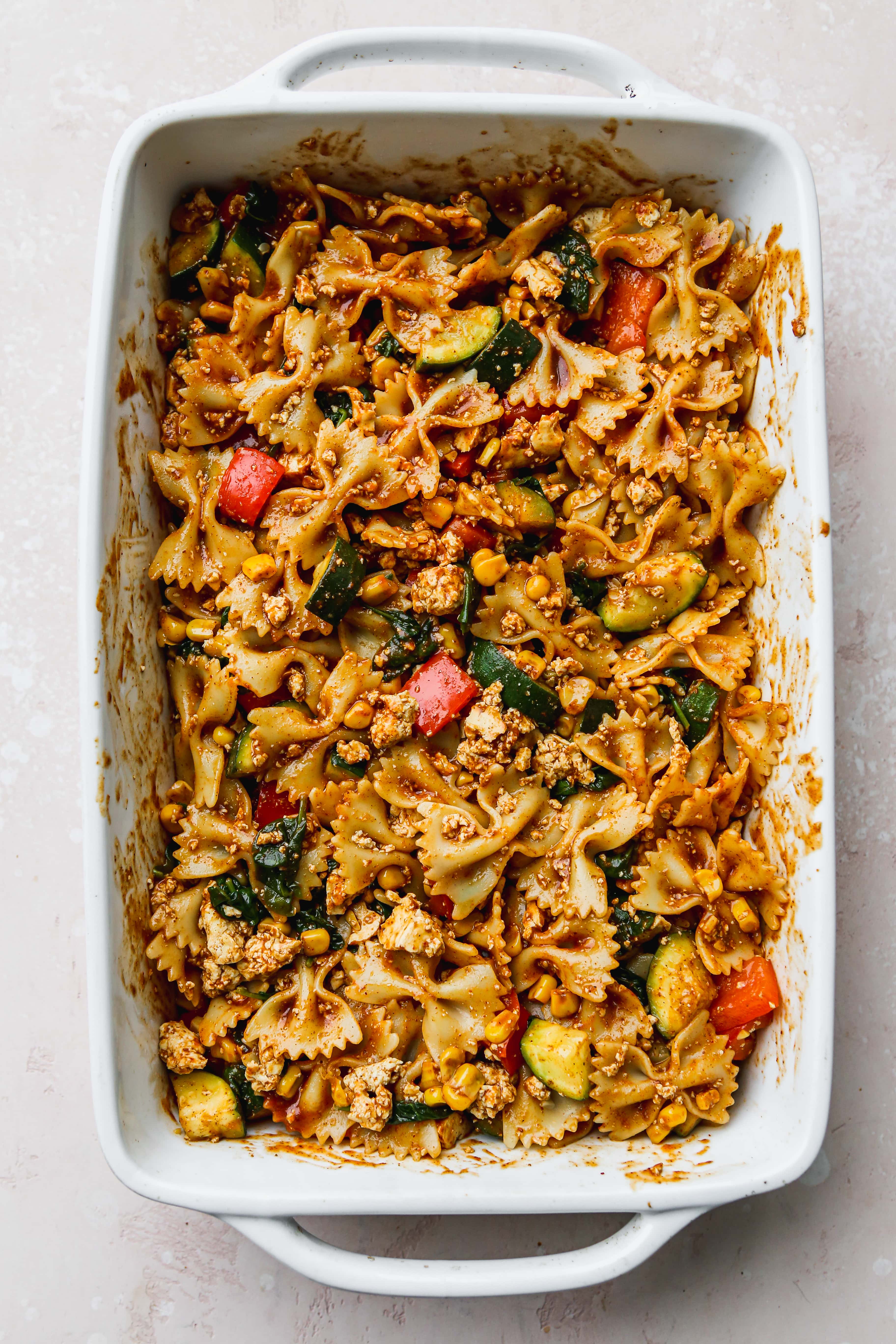 Bowtie pasta tossed in cooked vegetables and taco sauce in a large baking dish.