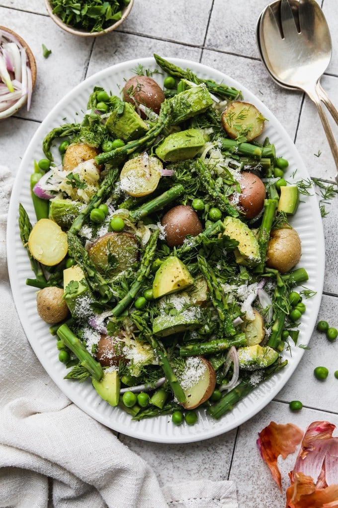 Asparagus salad with potatoes, peas, and avocados on a white plate.
