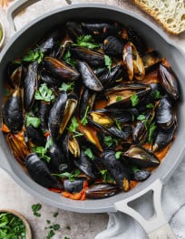 A large pan with steamed mussels in tomato coconut curry.