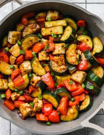 Zucchini stir fry with bell peppers, carrots, and tofu in a large pan.