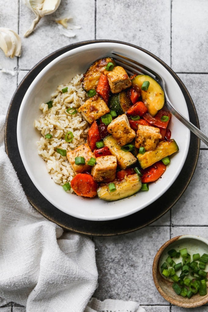 Zucchini stir fry with bell peppers, carrots, and tofu in a bowl over rice.