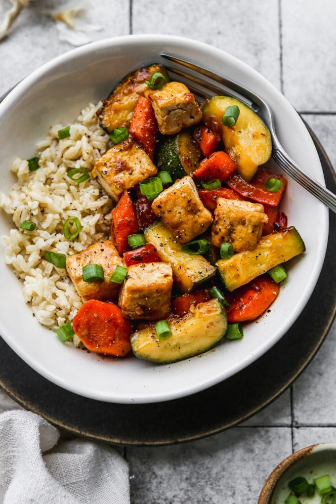 Zucchini stir fry with bell peppers, carrots, and tofu in a bowl over rice.