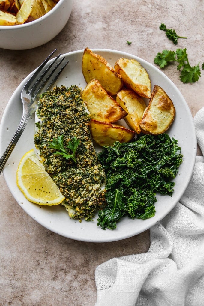 Herb crusted cod with potatoes and kale on a white plate.