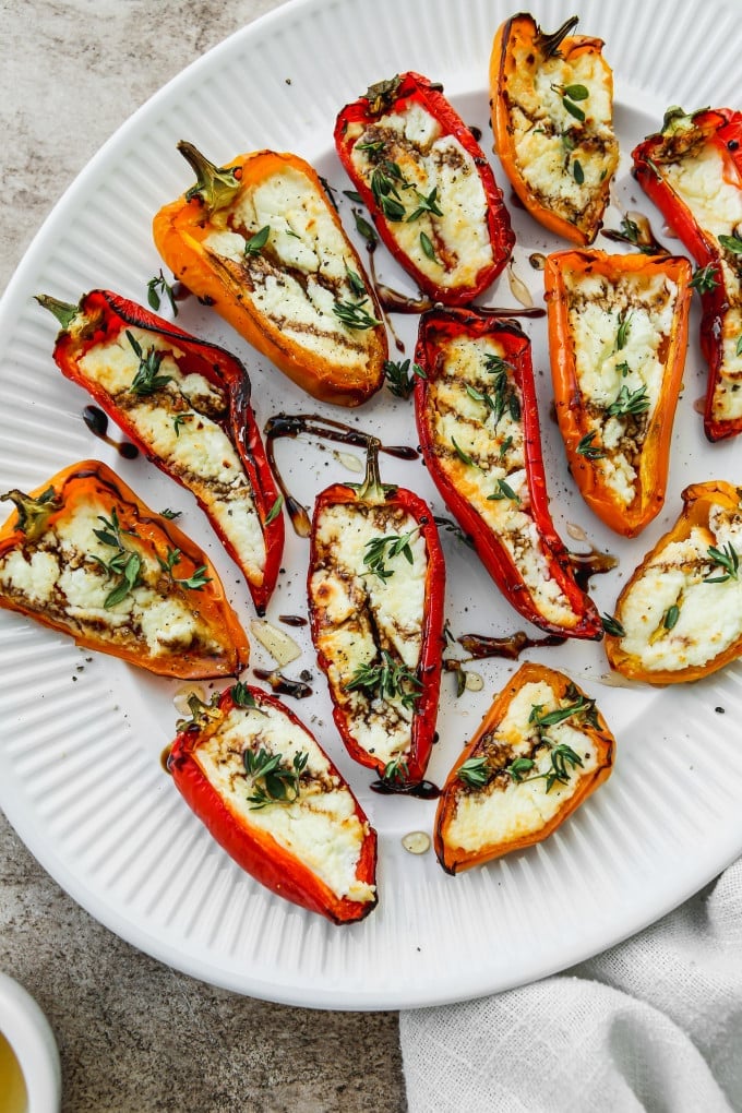 Roasted goat cheese stuffed mini peppers drizzled with balsamic, honey, and thyme on a white plate.