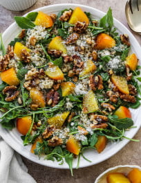 Golden beet salad with arugula, quinoa, walnuts, and parmesan on a white plate.