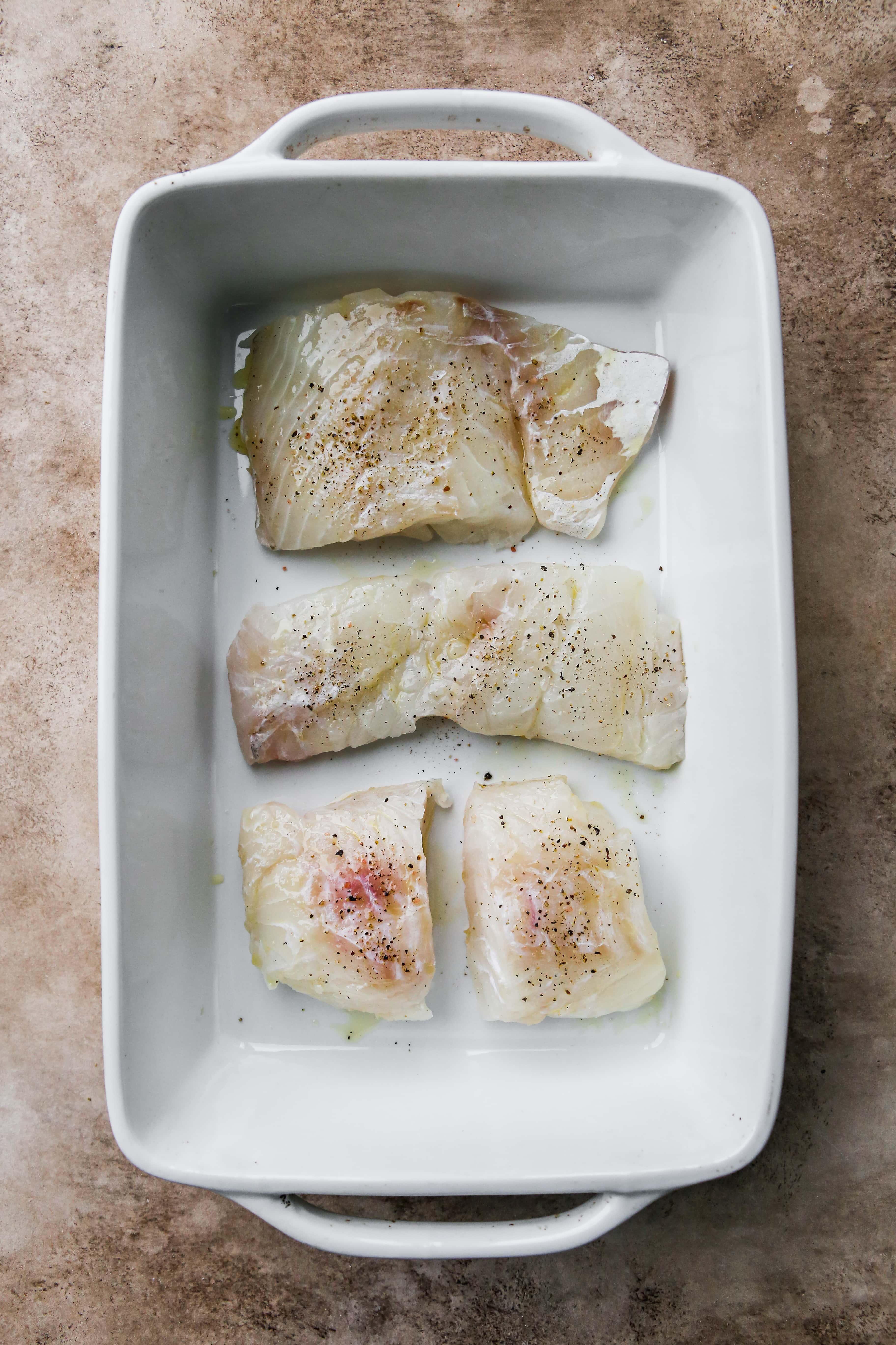 Uncooked cod fillets in a white baking dish.