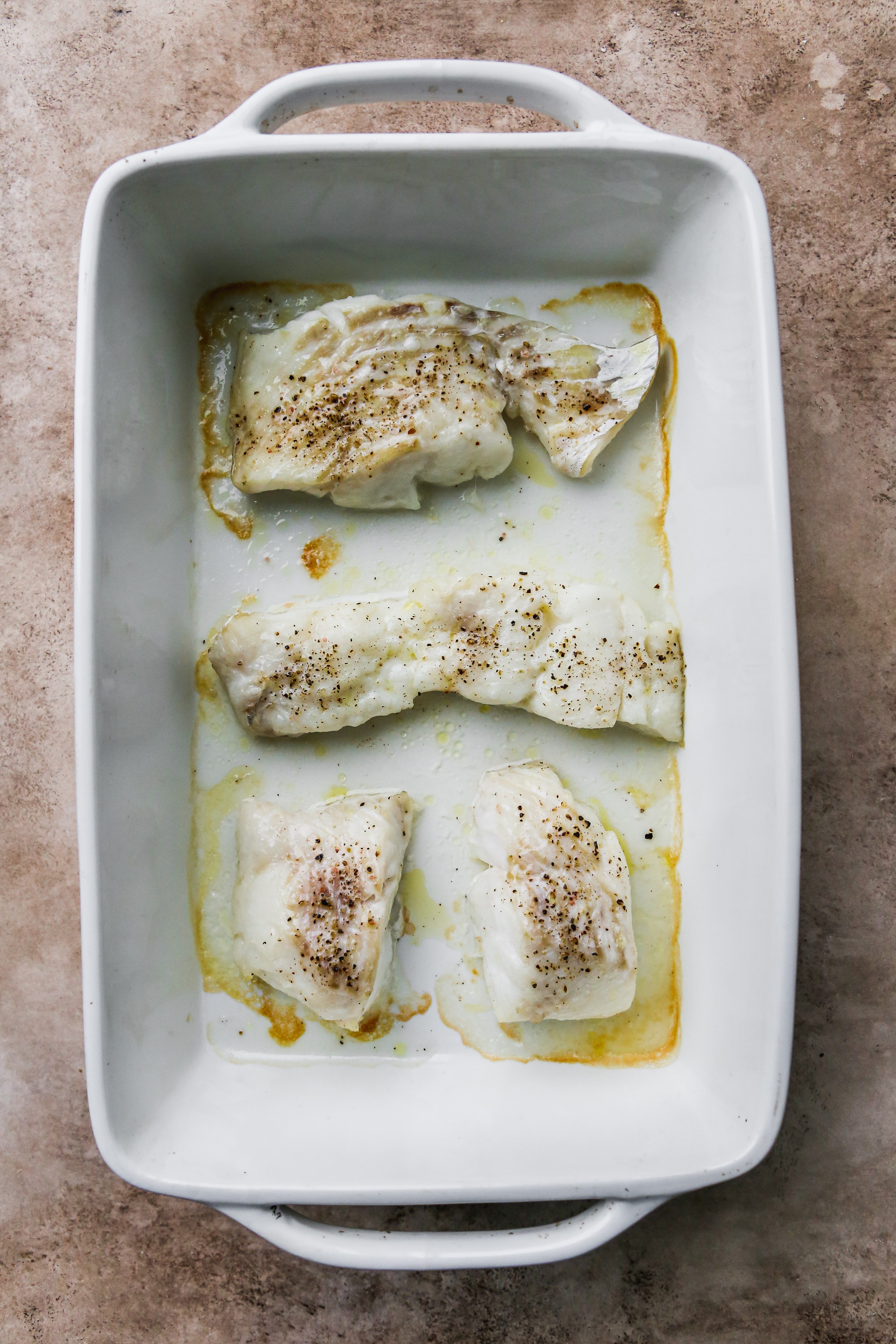 Baked cod fillets in a white baking dish.