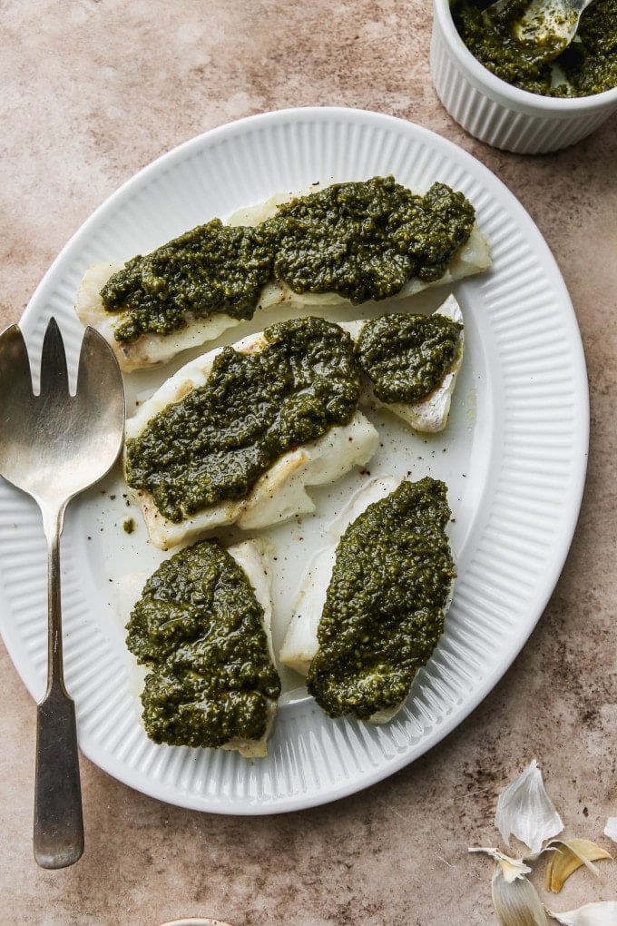 Baked pesto cod fillets on a white serving tray.