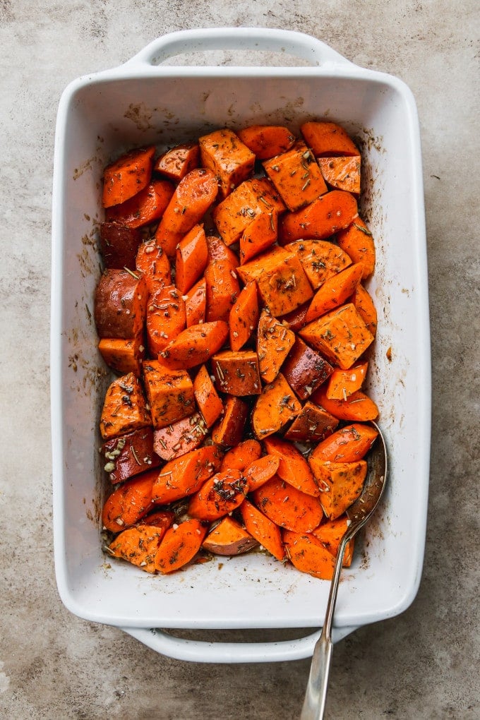 Chopped sweet potatoes and carrots tossed in seasonings in a baking dish.