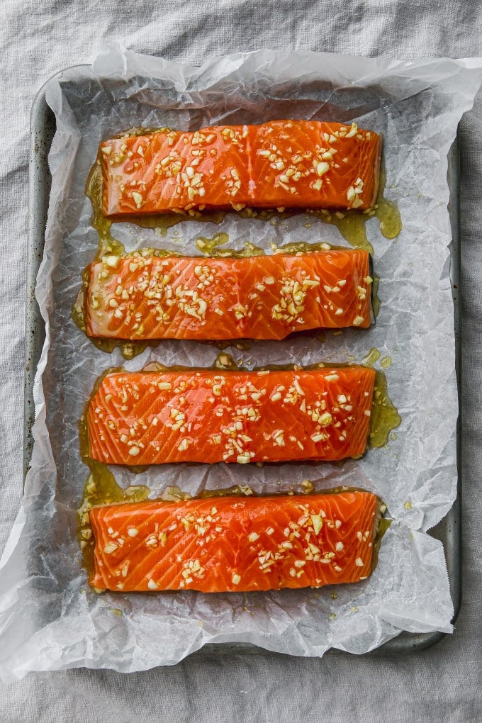 4 fillets of salmon topped with olive oil, honey, and garlic mixture on a baking sheet.
