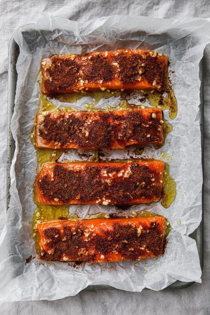 4 fillets of salmon topped with chili powder and olive oil, honey, and garlic mixture on a baking sheet.