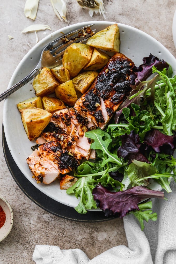 A serving of baked chili salmon with potatoes and salad on a plate.