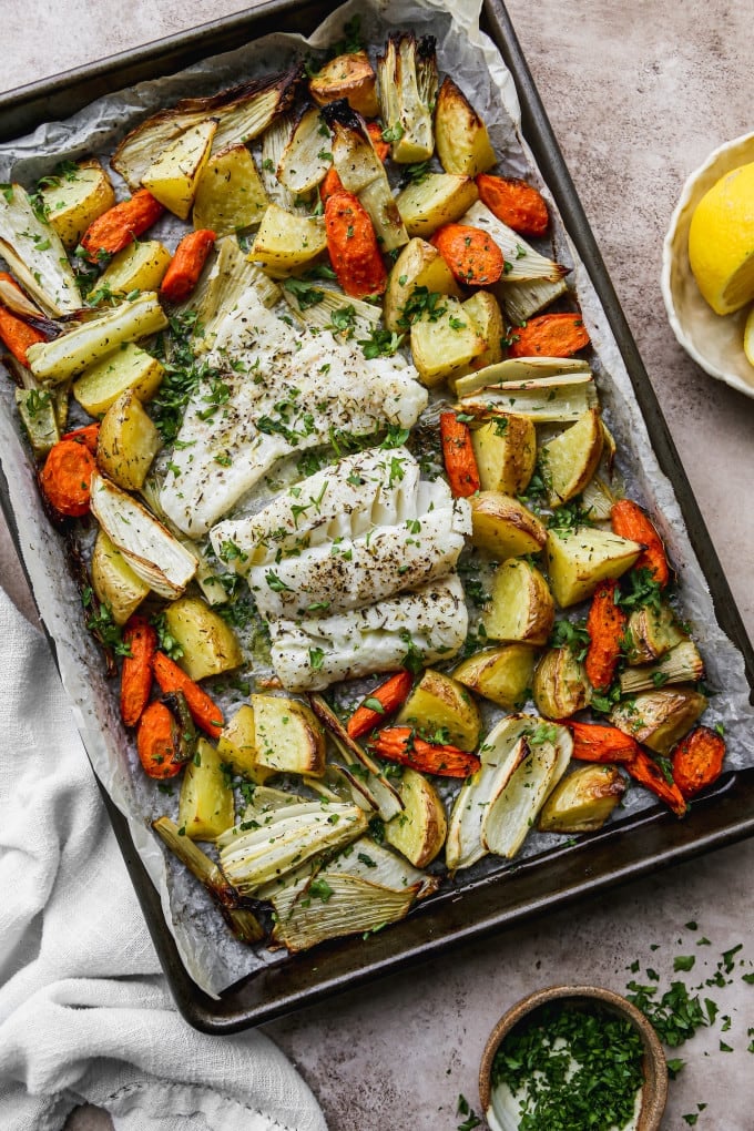 Baked cod fillets and vegetables on a sheet pan.