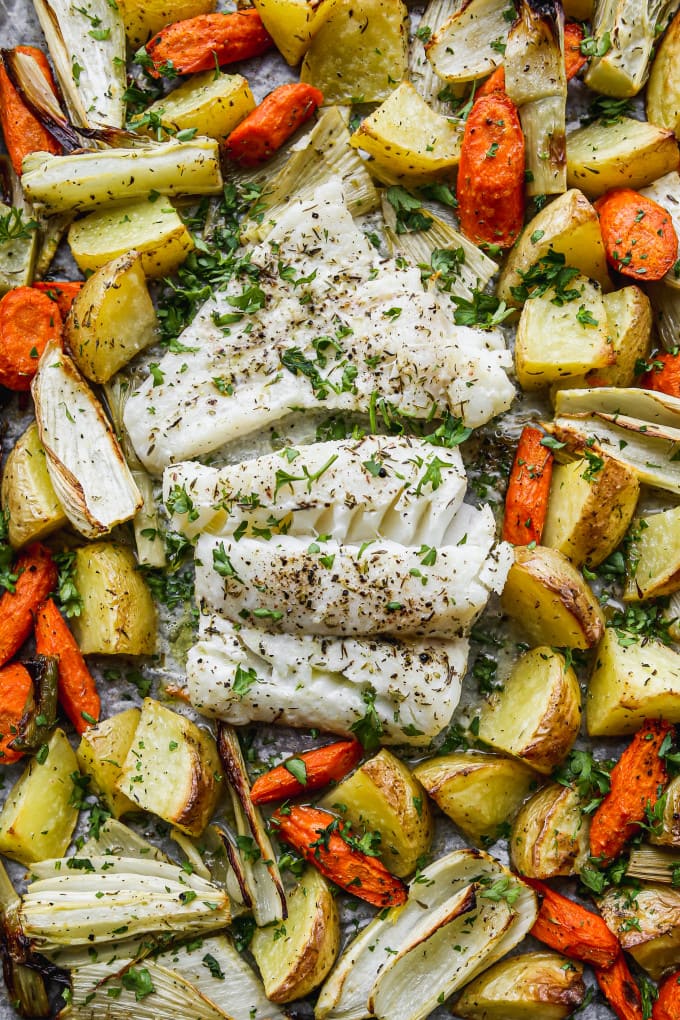 Closeup of baked cod fillets and vegetables on a sheet pan.