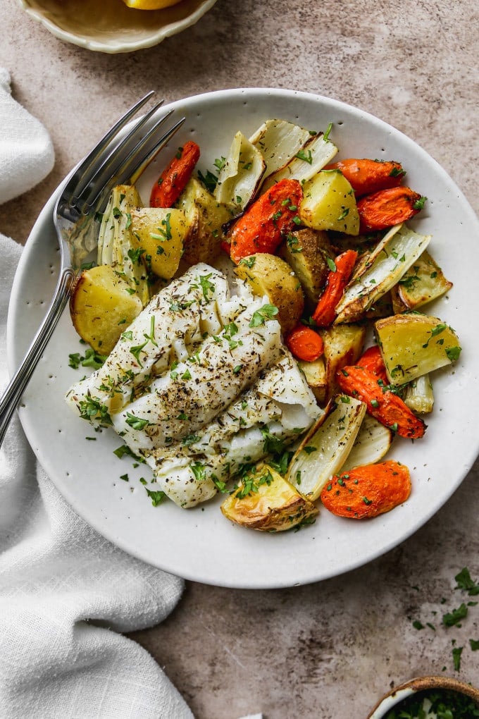Serving of baked cod and vegetables in a white bowl.