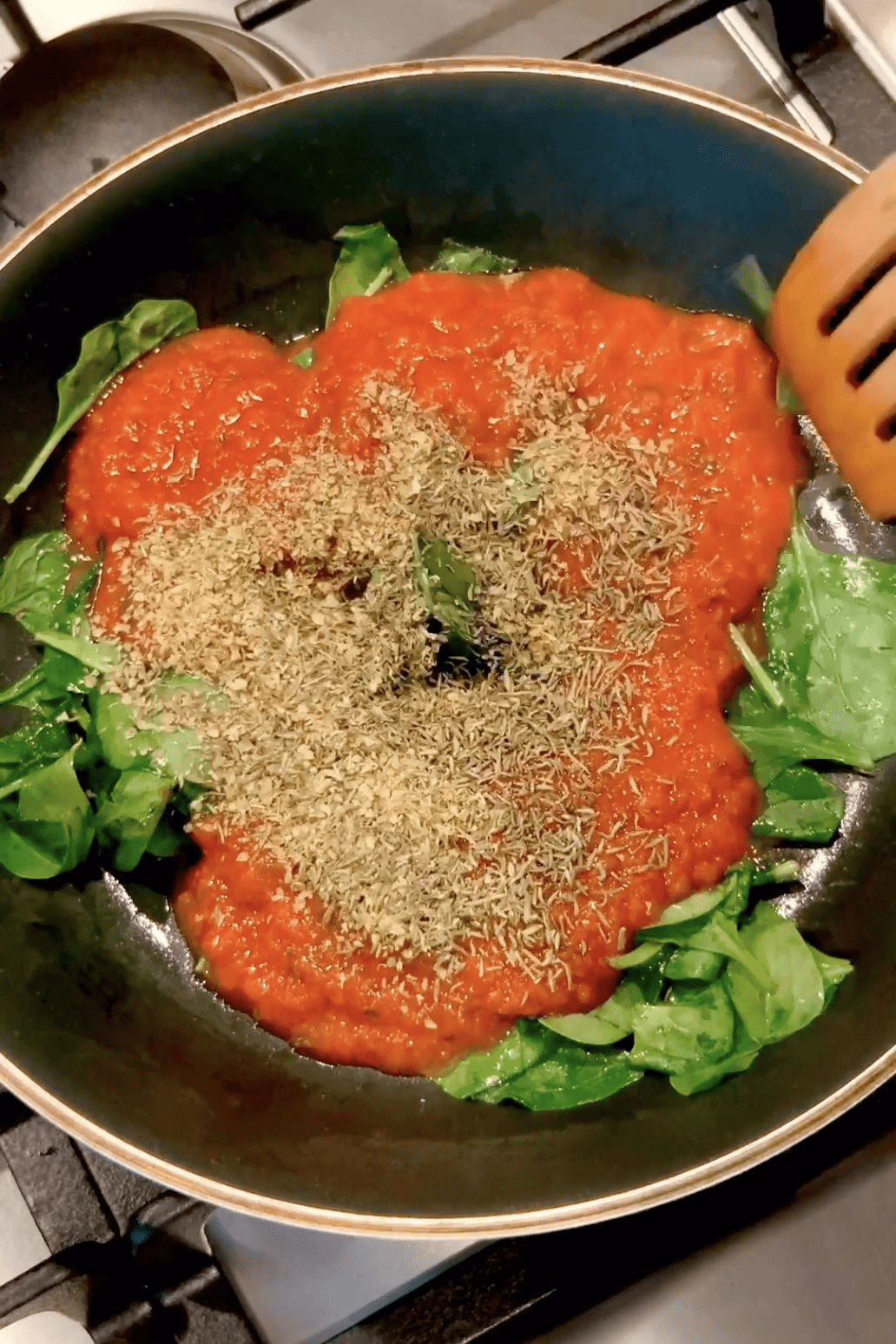 Tomato sauce and spices added to spinach on a pan.