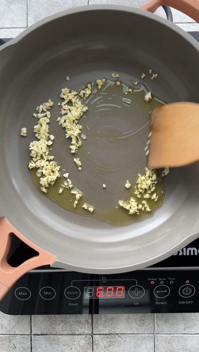 Cooking minced garlic in olive oil on a pan.