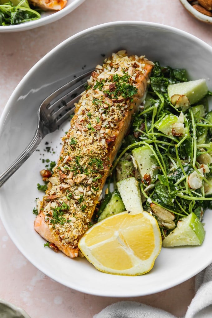 Almond crusted salmon plated with lemon and a side salad.
