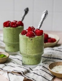 Matcha overnight oats in two small jars, topped with raspberries.