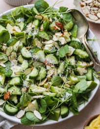 Watercress salad with apples, cucumber, pecorino, and almonds on a white plate.