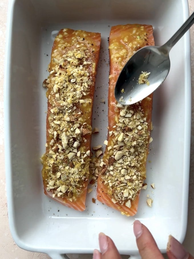 Salmon fillets topped with almond crust in a baking dish.