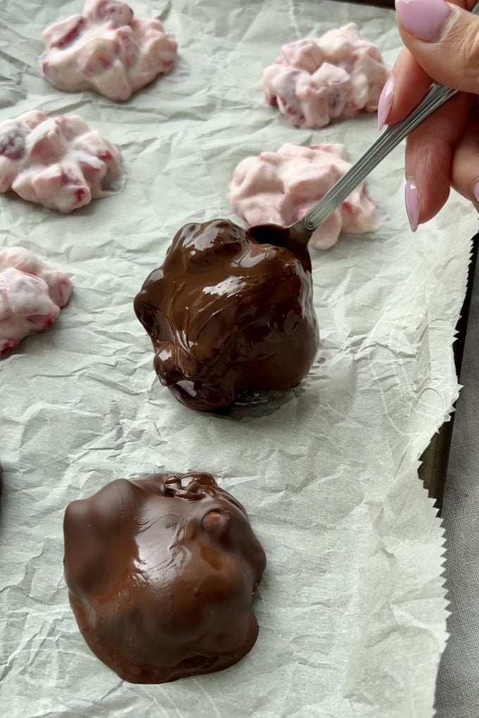 Placing chocolate strawberry yogurt clusters on a baking sheet for cooling.