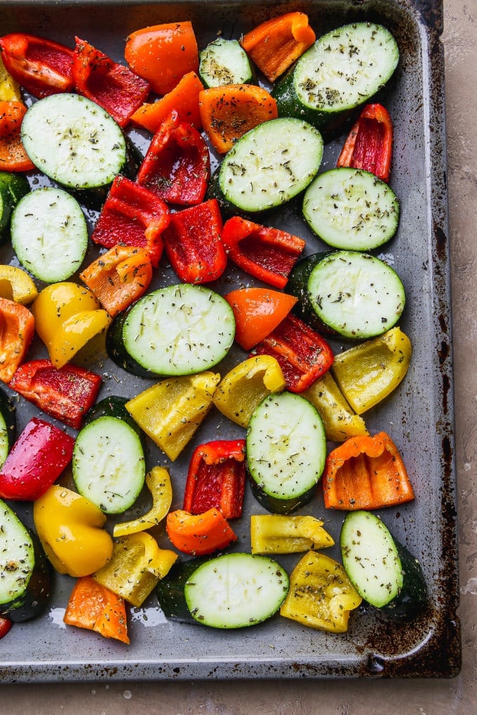 Sliced zucchini and peppers tossed in olive oil and herbs on a sheet pan.
