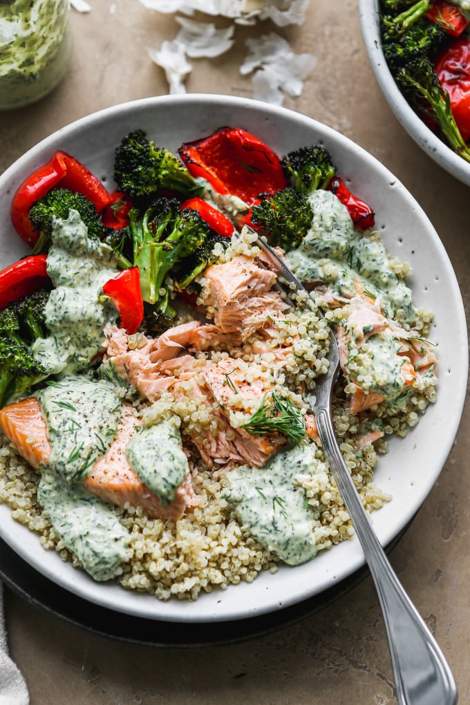 Salmon quinoa bowl with roasted veggies and tahini sauce mixed together.