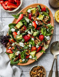 Strawberry salad with walnuts, goat cheese, basil, and avocado on a serving plate.