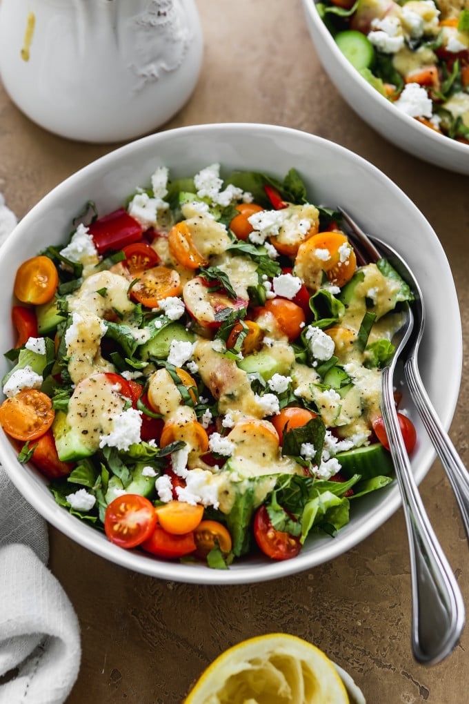 Chopped green salad topped with creamy hummus dressing in a white bowl.