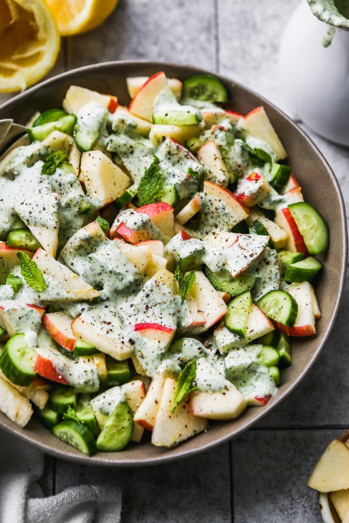 Apple cucumber salad topped with minty yogurt dressing in a large bowl.