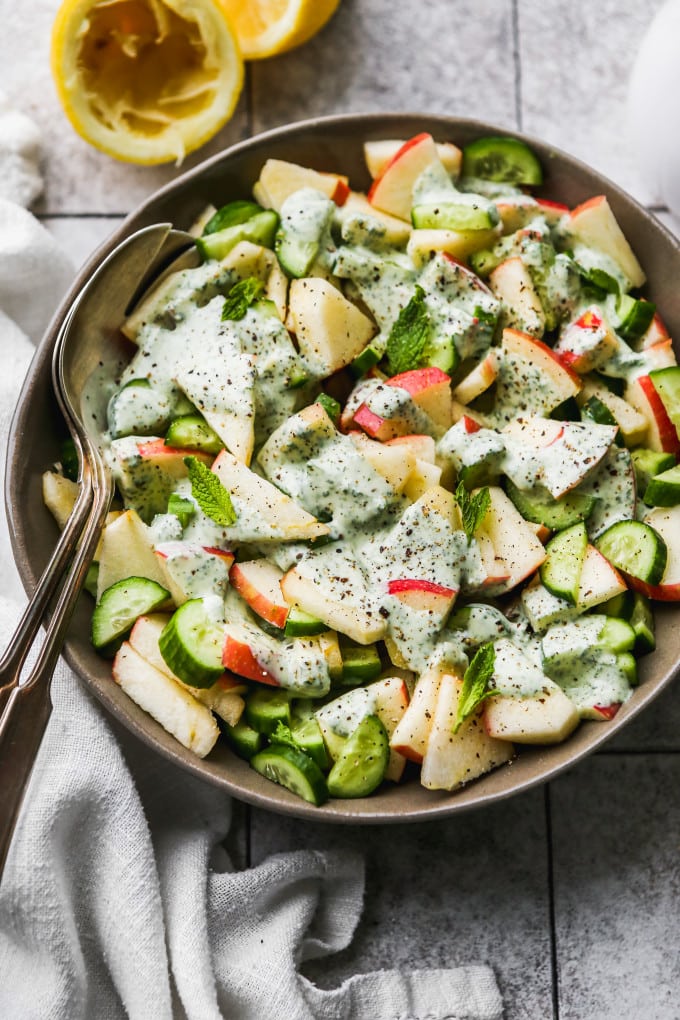 Apple cucumber salad topped with minty yogurt dressing in a large bowl.