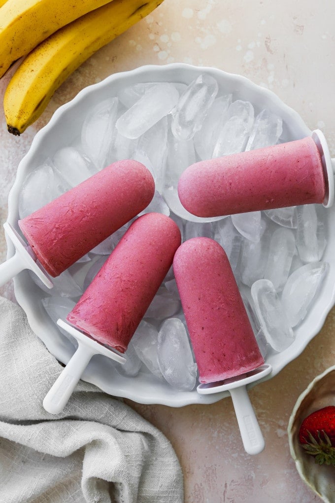 Strawberry banana yogurt popsicles displayed on a bowl of ice.