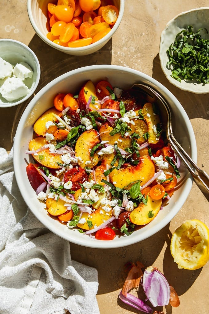 Peach feta salad with tomatoes, shallots, and herbs in a white bowl.