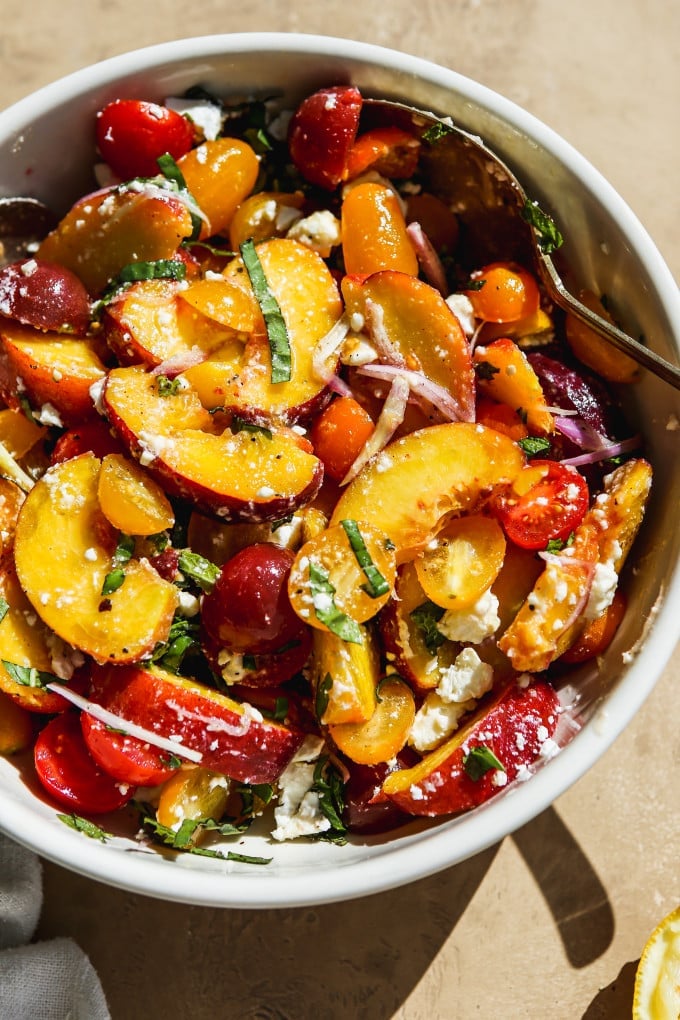 Peach feta salad tossed in salad dressing in a large bowl.