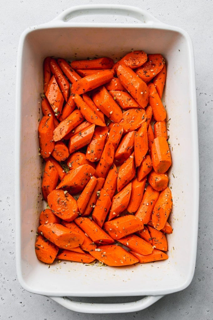Uncooked carrots tossed in oil, honey, garlic, and spices in a baking dish.