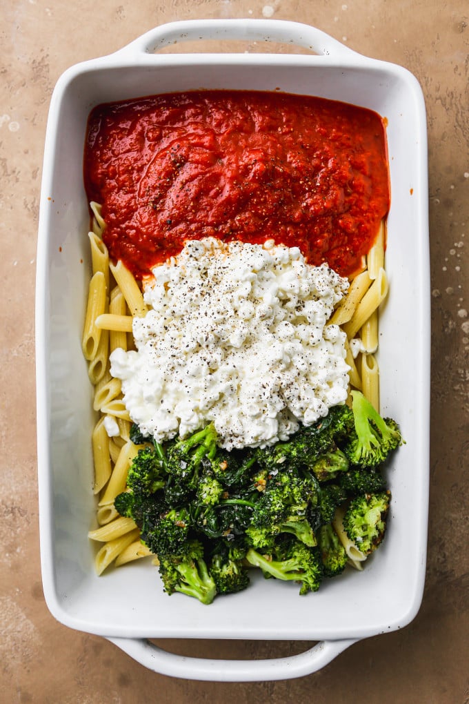 Cooked pasta, tomato sauce, cottage cheese, and veggies in a large baking dish.