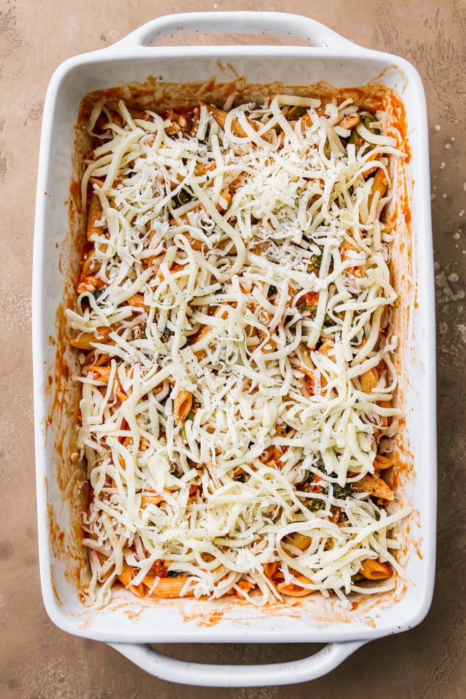 Pasta bake ingredients topped with shredded mozzarella in baking dish.