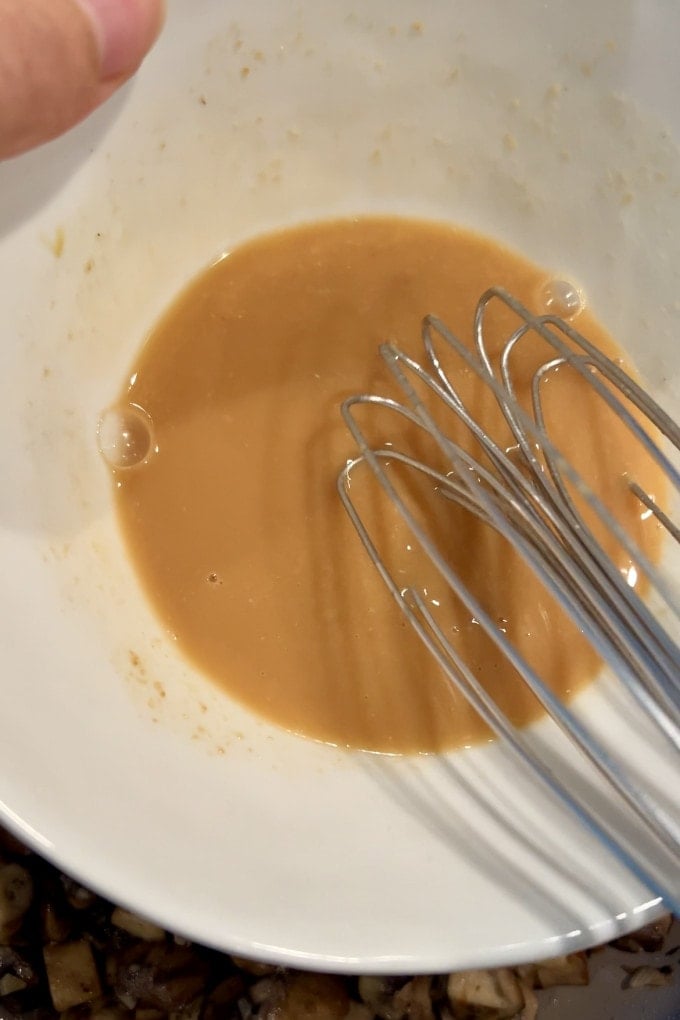 Whisking miso paste with pasta water in a bowl.