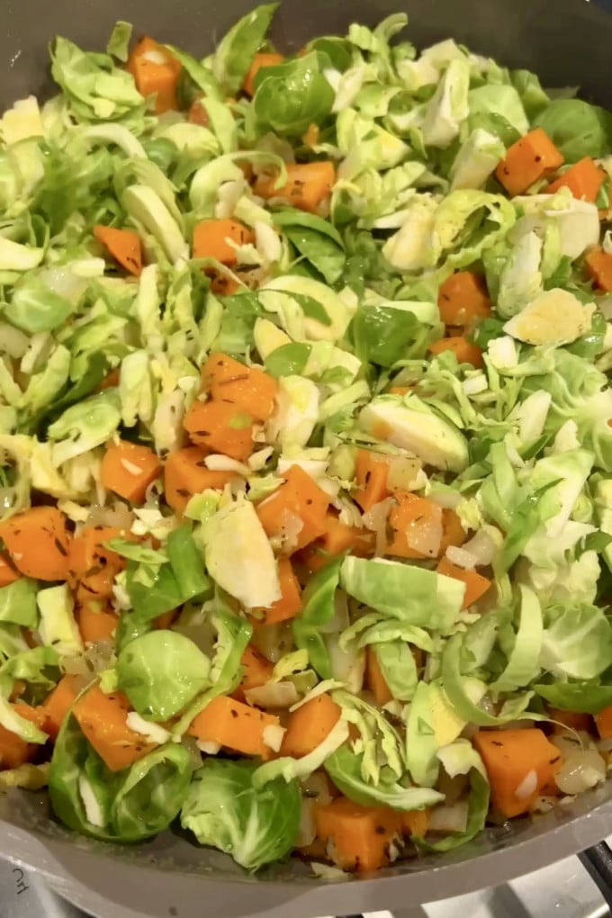 Adding shredded brussels sprouts to sweet potatoes in pan.