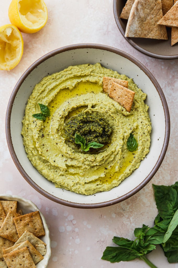 Pesto hummus recipe served in a bowl with crackers.