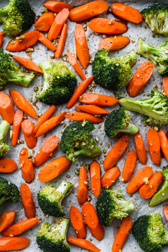 Seasoned broccoli florets and sliced carrots on a baking sheet.